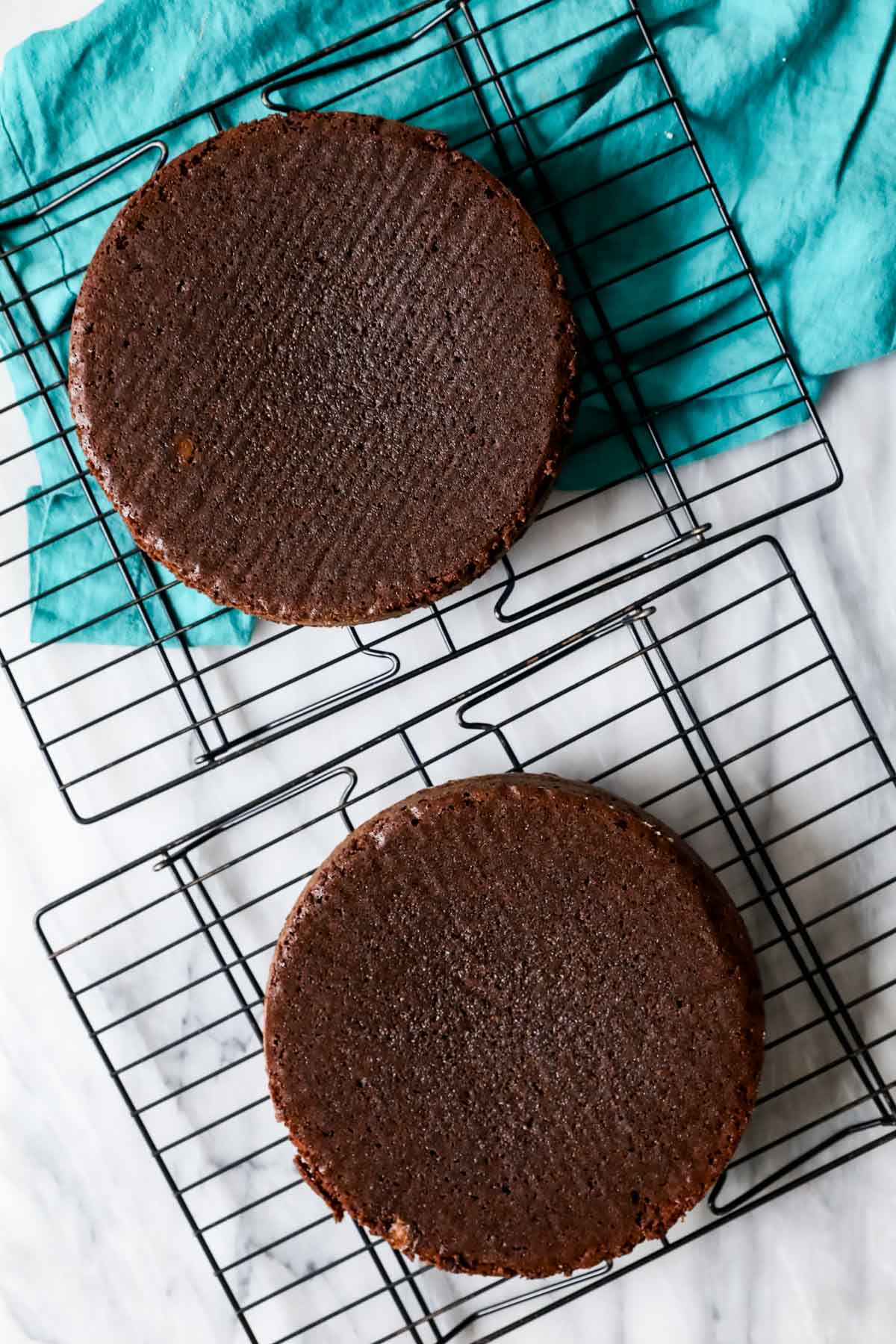 Two round, freshly baked chocolate cake layers on cooling racks.