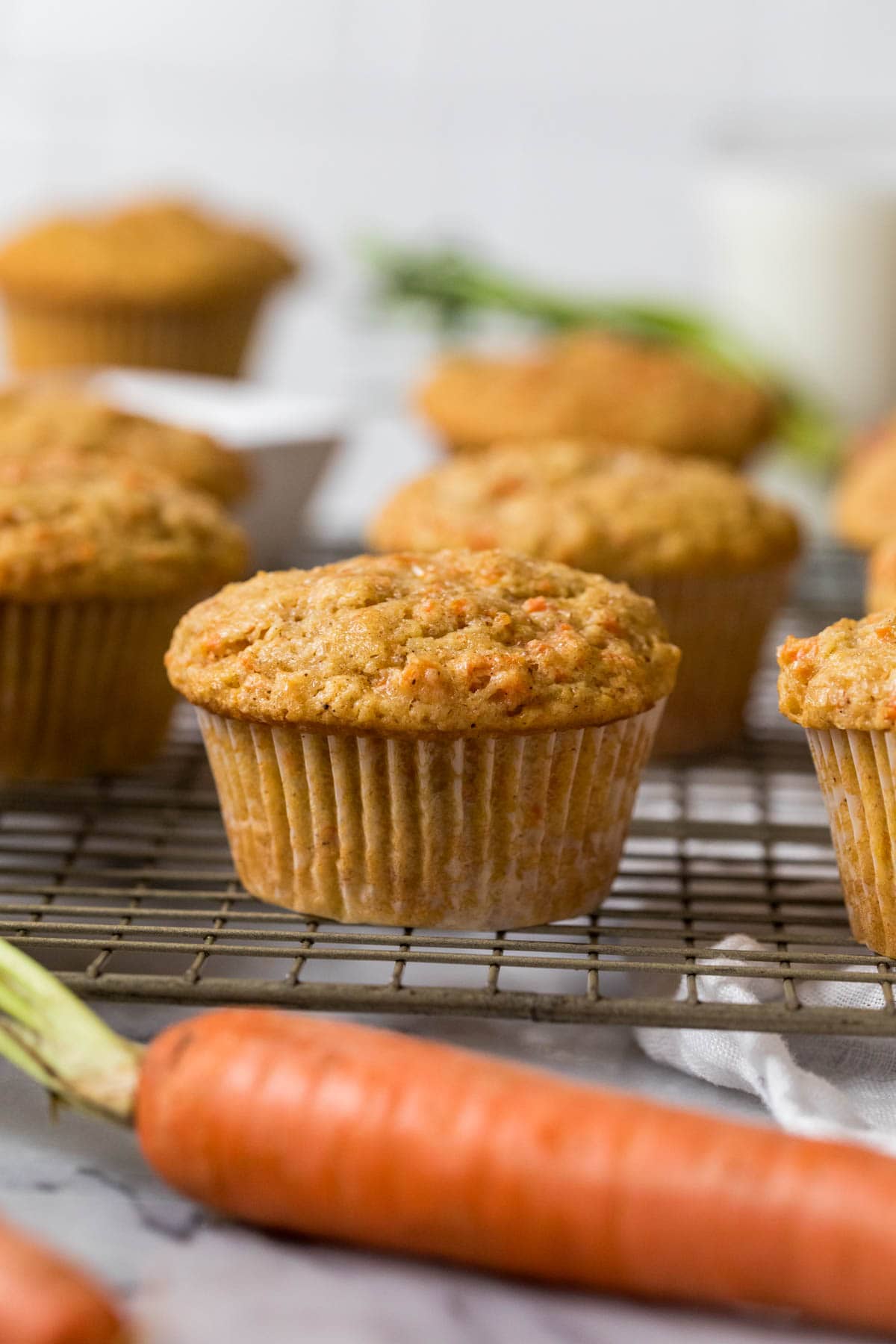 Muffins on a cooling rack with a carrot in the foreground.