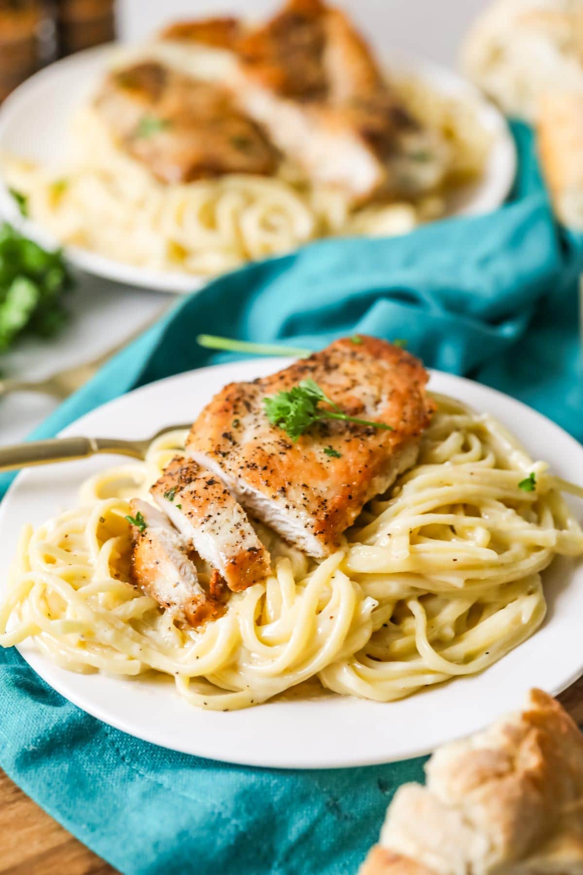 Plate of pasta topped with alfredo sauce and a seared chicken breast that's been cut into two bites.
