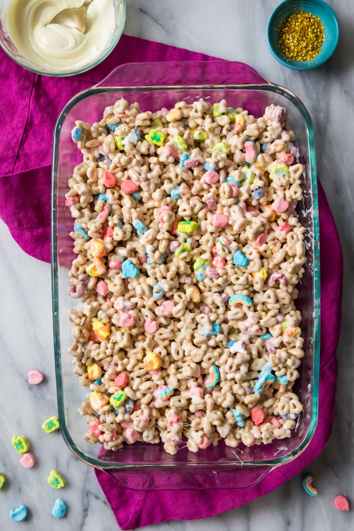 Overhead view of a mixture of lucky charms cereal and melted marshmallow in a glass casserole dish.
