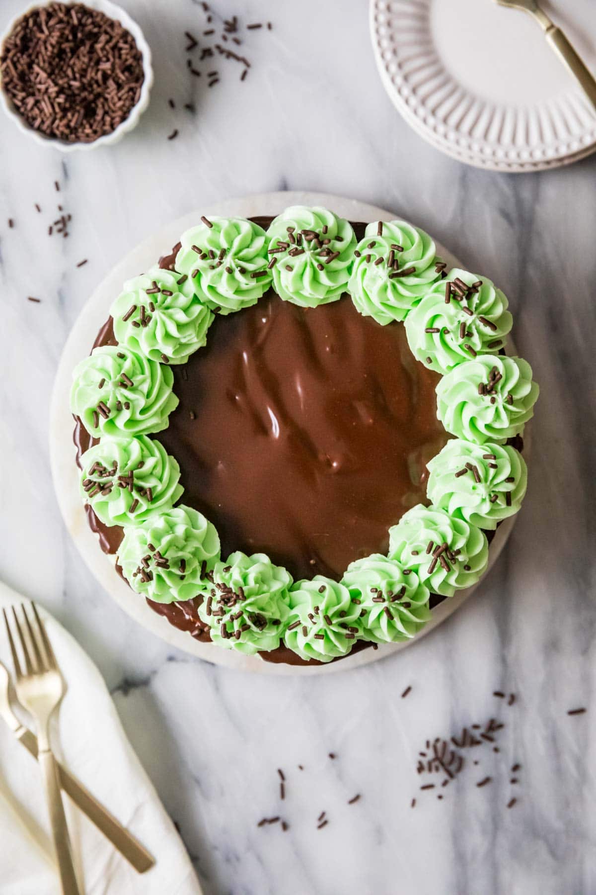 Overhead view of a cake topped with chocolate ganache and piped mint frosting swirls.