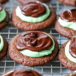 Mint chocolate cookies made with a chocolate cookie base, mint frosting, and chocolate ganache on a cooling rack.