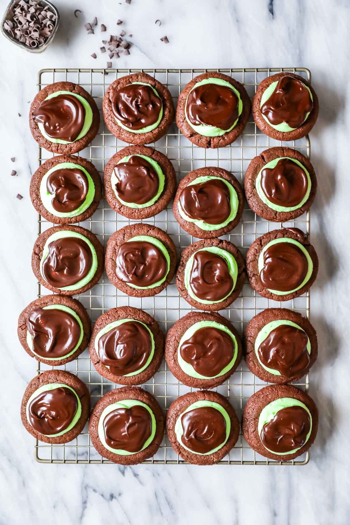 Overhead view of rows of chocolate cookies topped with mint frosting and chocolate ganache.