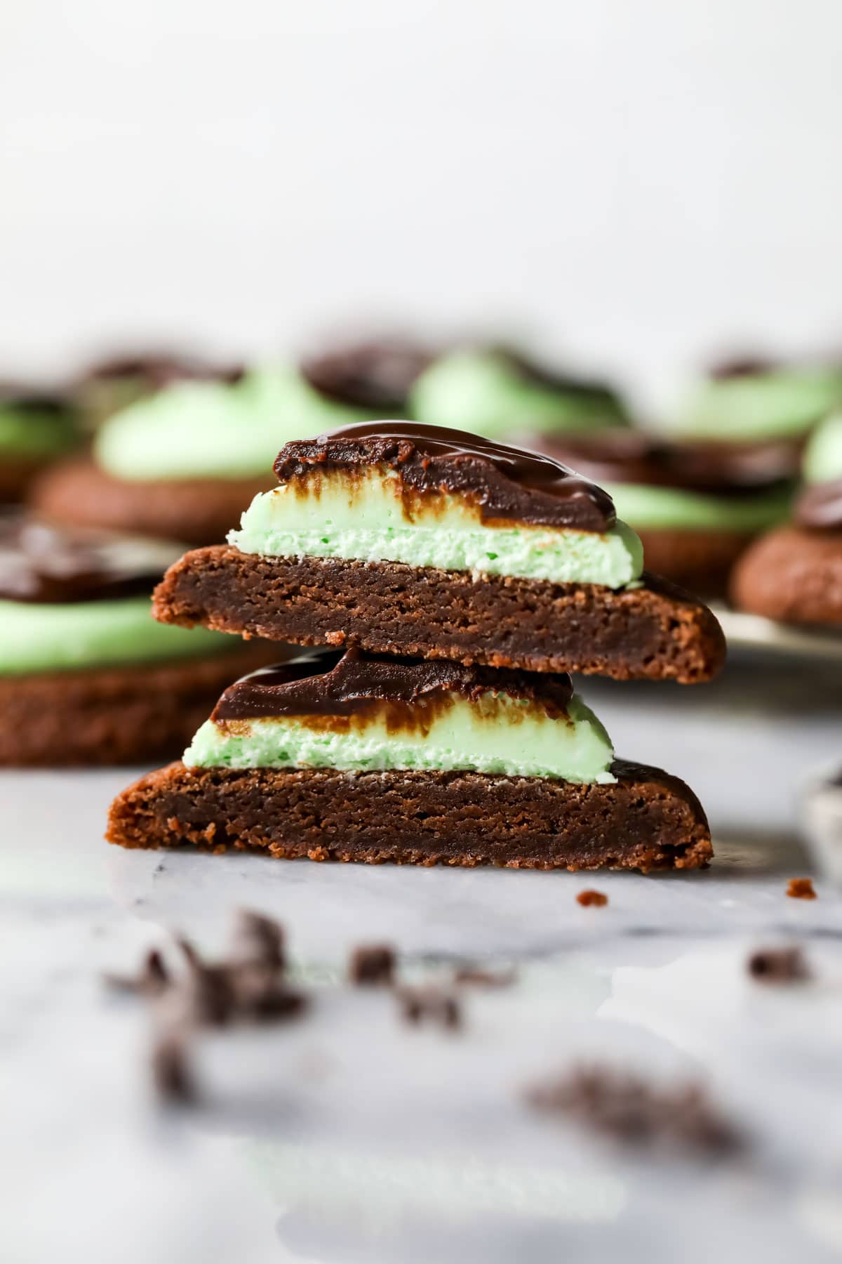 Two halves of a mint chocolate cookie made with a chocolate cookie base, mint frosting, and chocolate ganache stacked on top of each other.