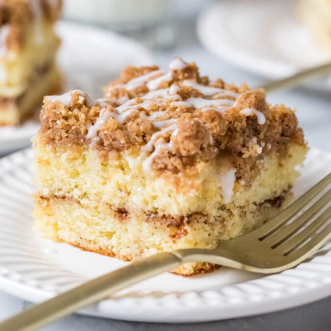 Slice of sour cream coffee cake with a fork on a white plate.