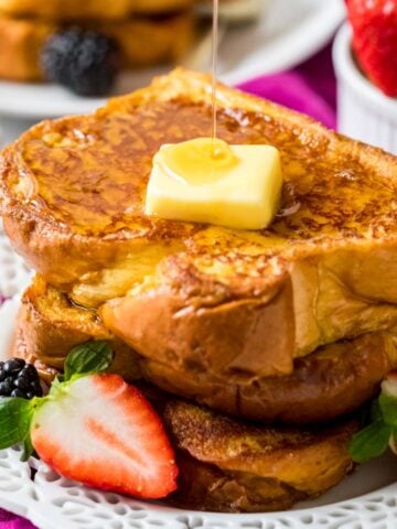 Stack of brioche french toast topped with a pat of butter and a drizzle of maple syrup.
