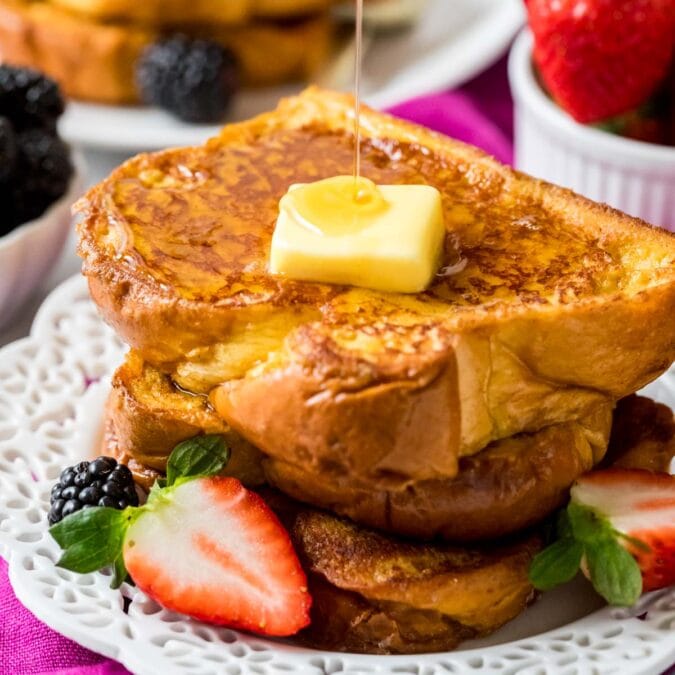 Stack of brioche french toast topped with a pat of butter and a drizzle of maple syrup.
