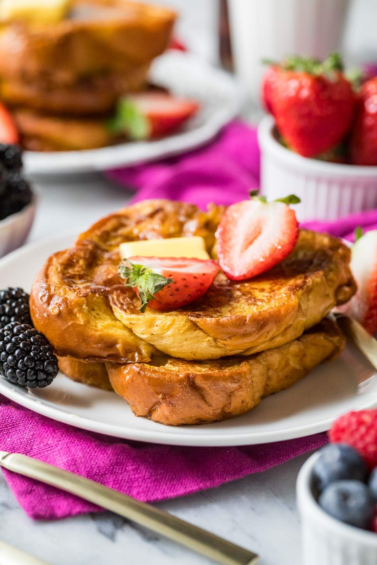 Stack of brioche french toast topped with a pat of butter and strawberry halves.