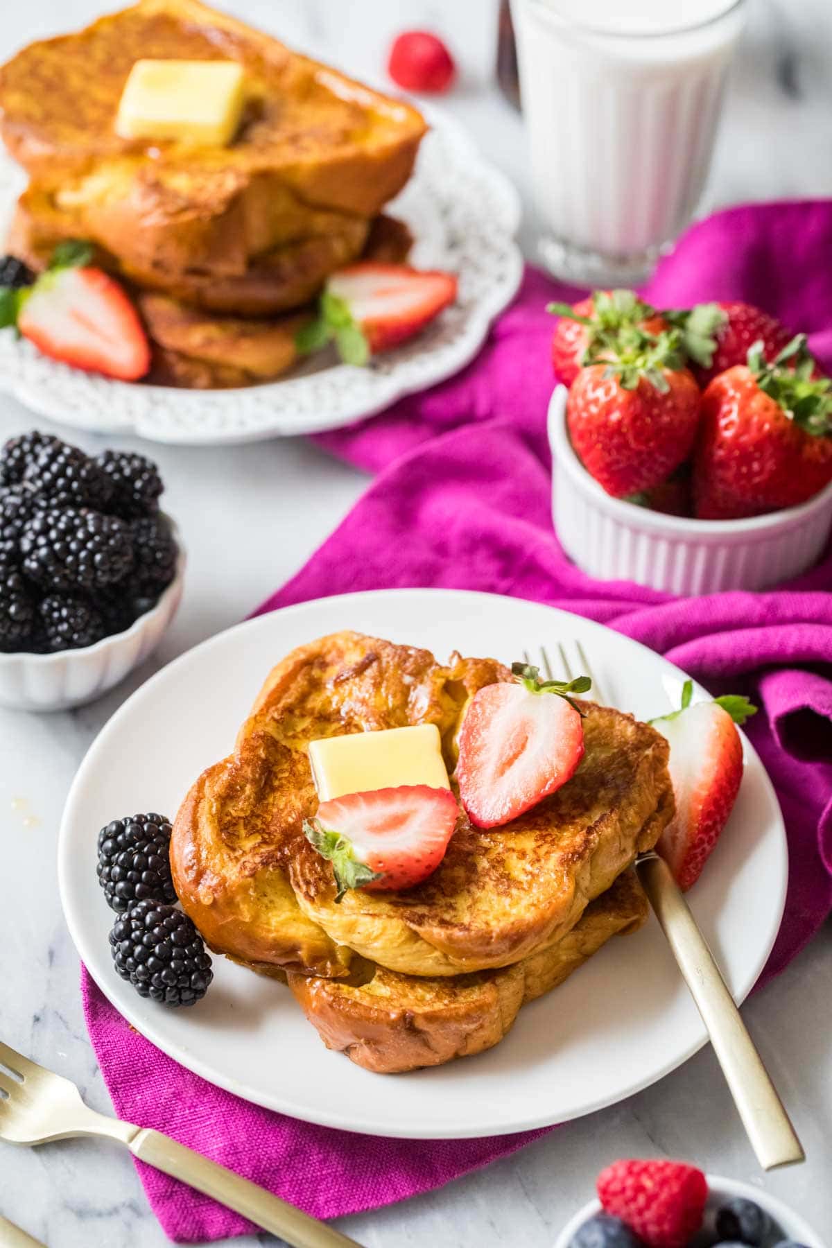 Stack of french toast made with brioche bread topped with a pat of butter and strawberry halves.