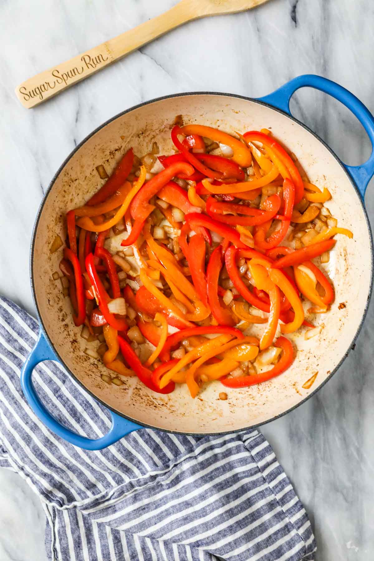 Overhead view of orange and red bell pepper strips sautéing in a pan.