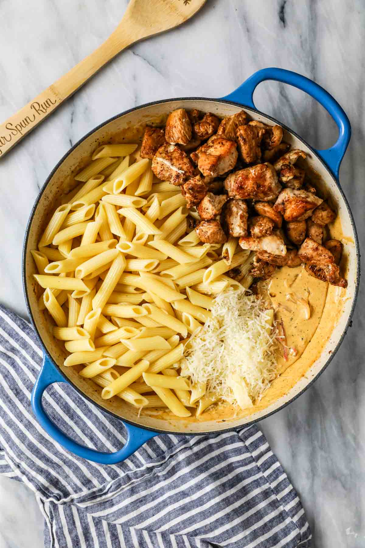 Overhead view of a saucepan with penne pasta, chicken, and parmesan cheese on top of a creamy sauce.