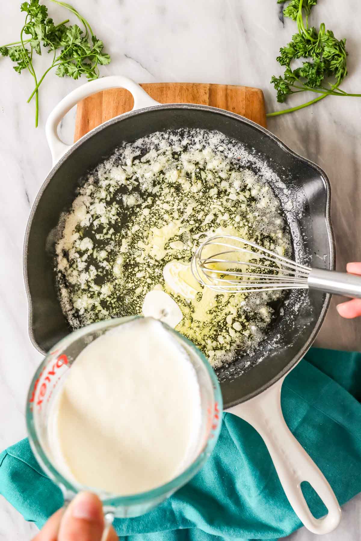 Cream being whisked into a pan of melted butter and garlic.