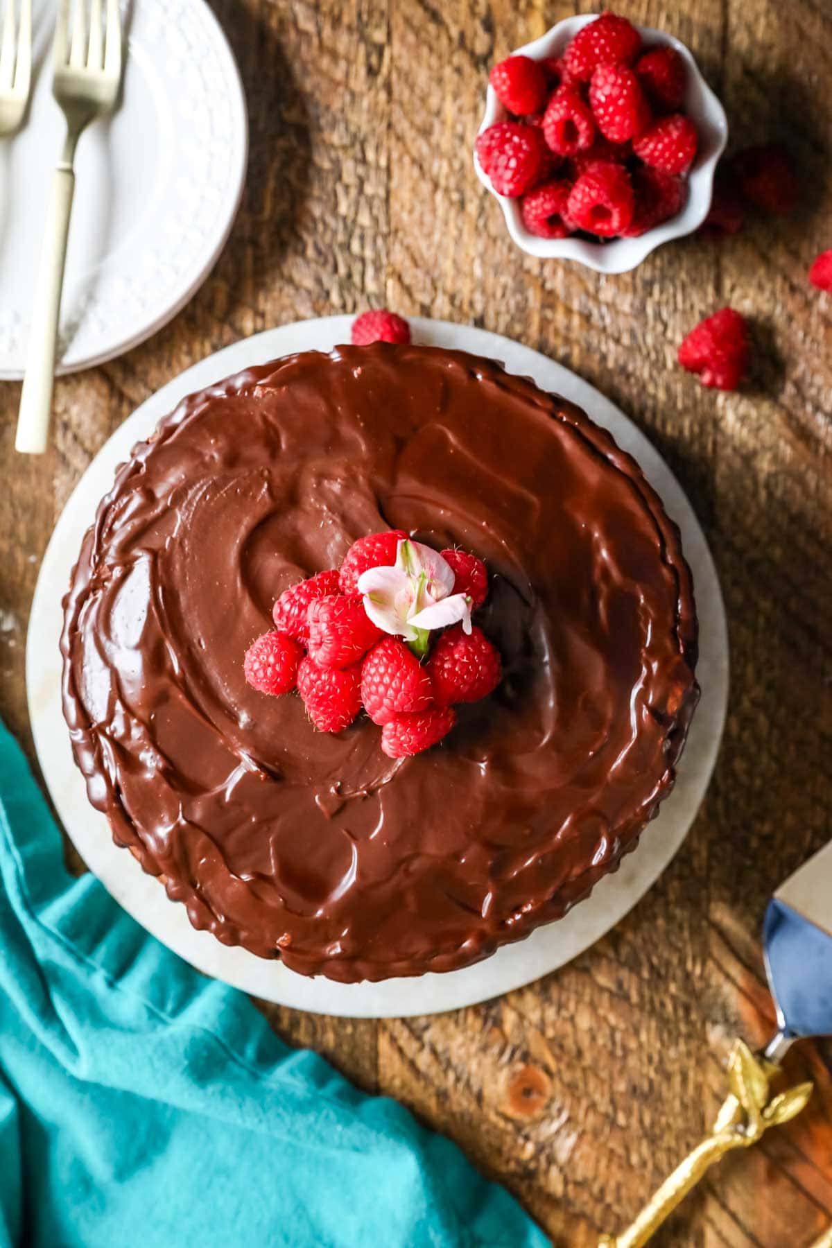 Overhead view of a cake topped with chocolate ganache and fresh raspberries.