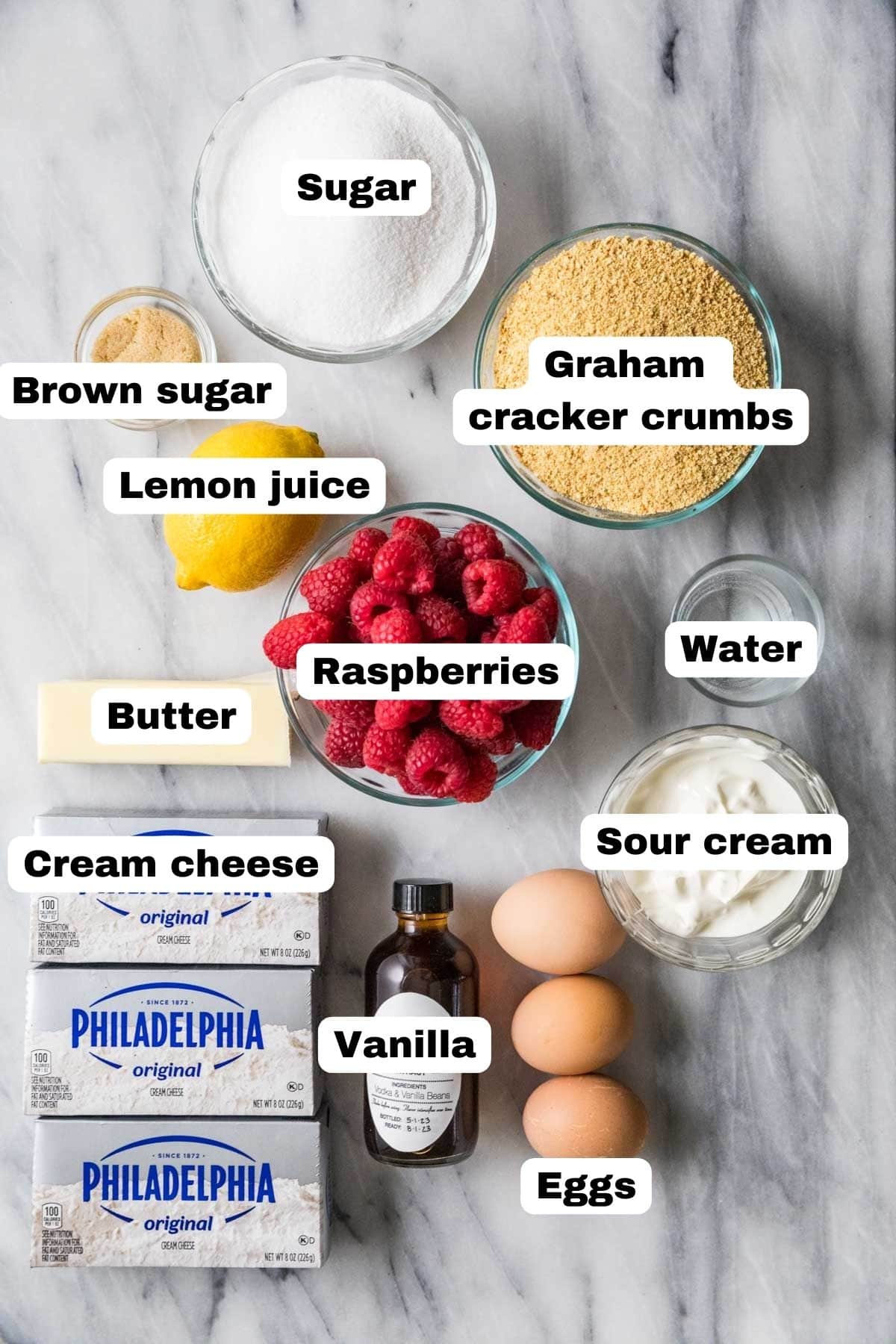 Overhead view of labelled ingredients including sour cream, raspberries, graham cracker crumbs, and more.