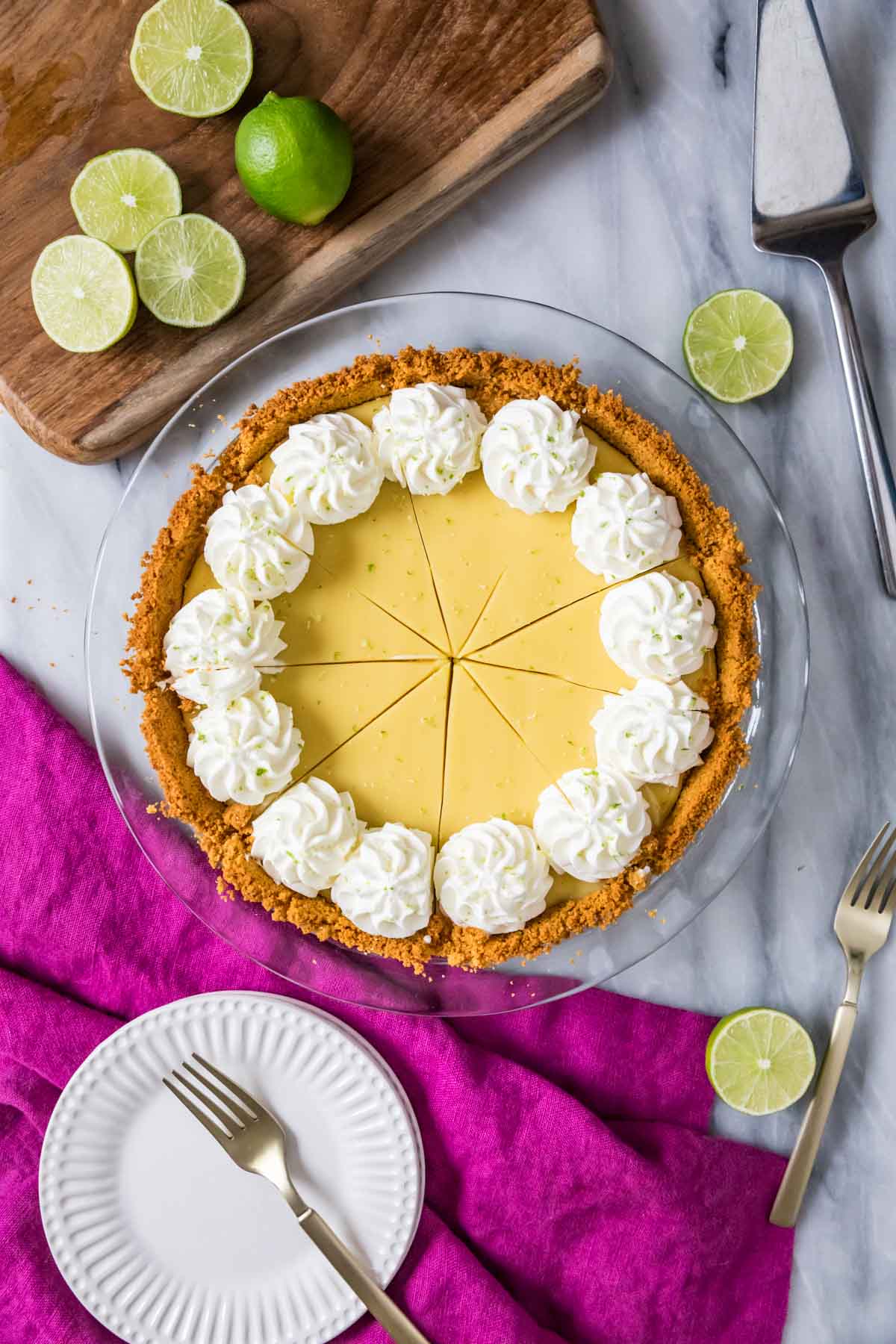 Overhead view of a pie that's been cut into slices and topped with swirls of whipped cream and lime zest.