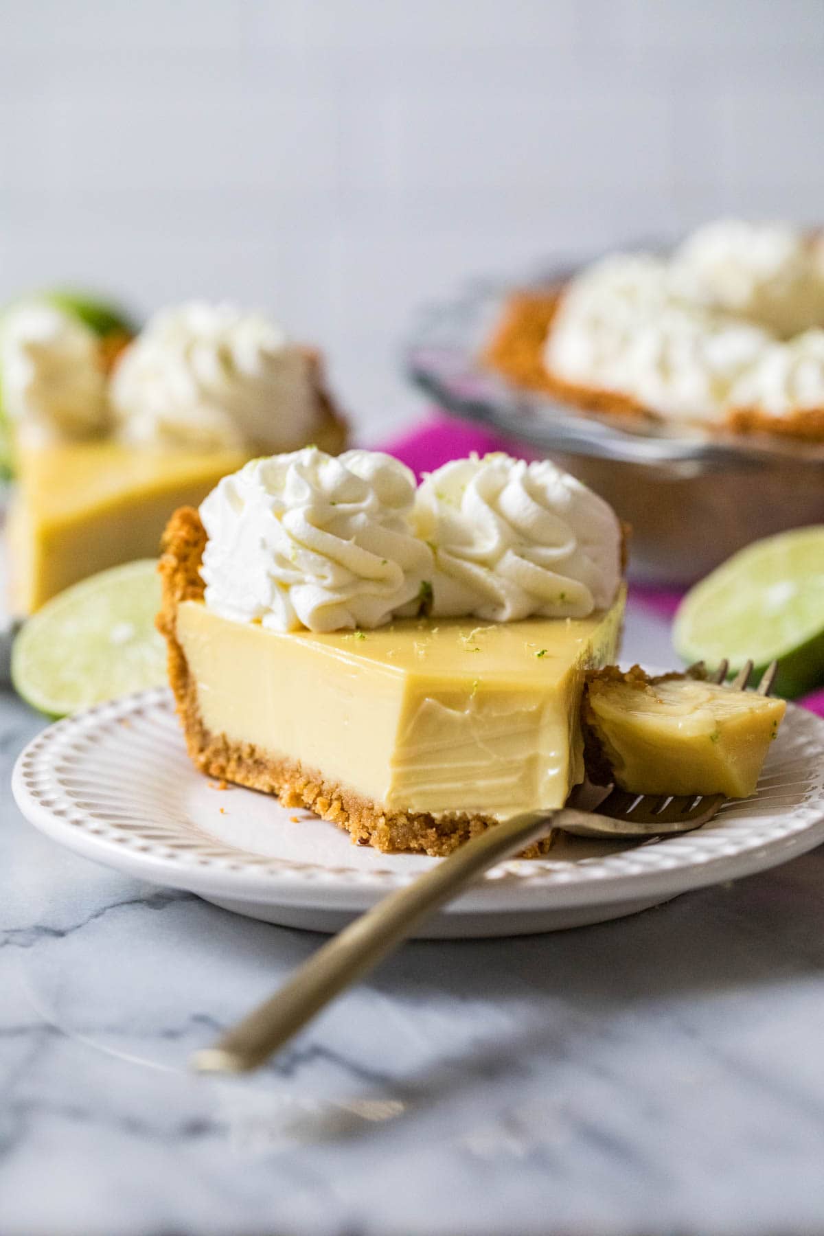 Slice of key lime pie with one bite that's sitting on a fork beside the pie.