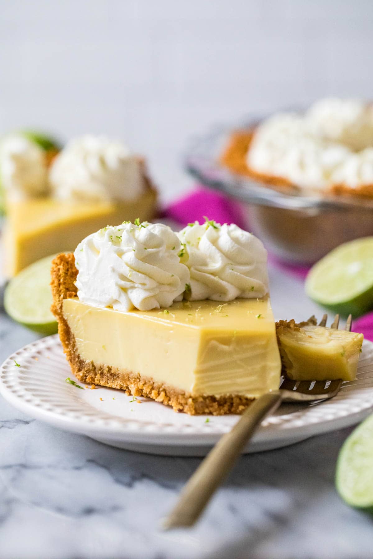 Slice of key lime pie with one bite that's sitting on a fork beside the pie.