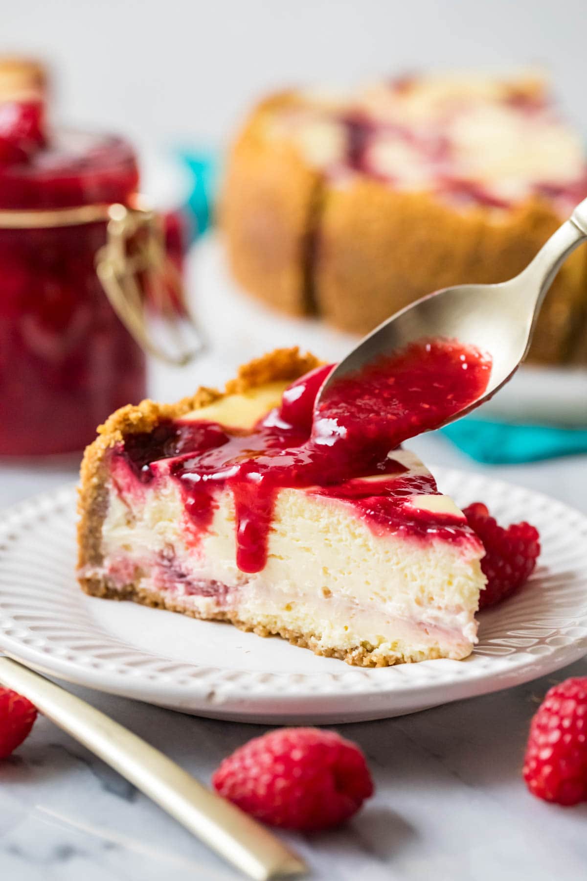 Raspberry sauce being poured over a slice of cheesecake.