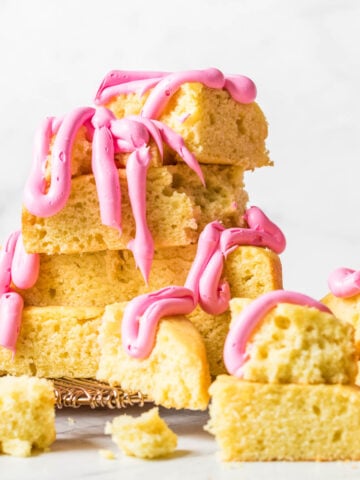 Hunks of yellow cake that have been stacked into a messy pile and drizzled with thick, bright pink frosting.