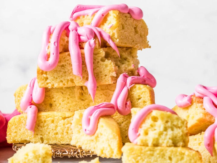 Hunks of yellow cake that have been stacked into a messy pile and drizzled with thick, bright pink frosting.