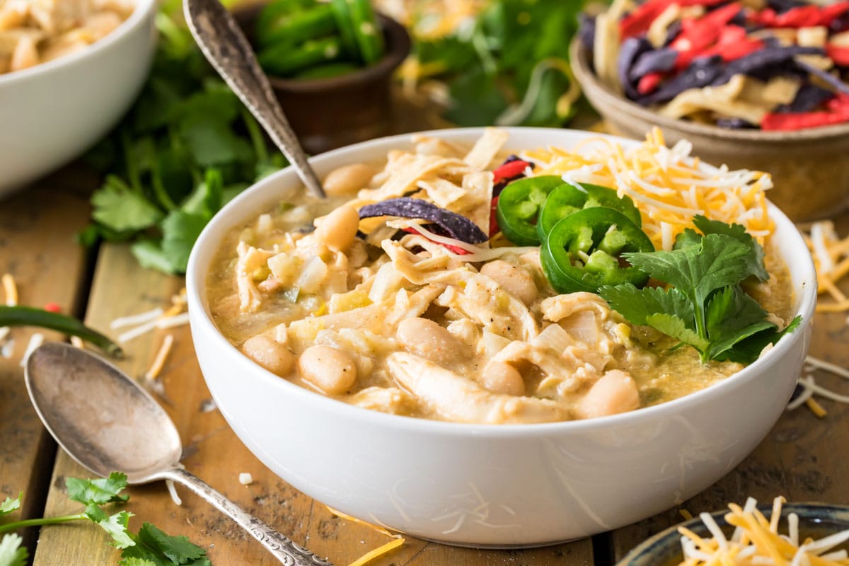 Bowl of white chili made with chicken and beans that's been topped with cilantro, jalapeno, tortilla strips, and cheese.