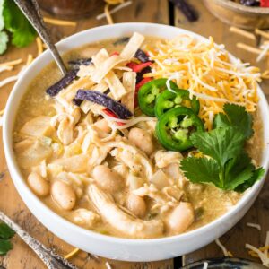 Bowl of white chicken chili topped with jalapeno, shredded tortillas, and cheese.