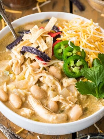 Bowl of white chicken chili topped with jalapeno, shredded tortillas, and cheese.