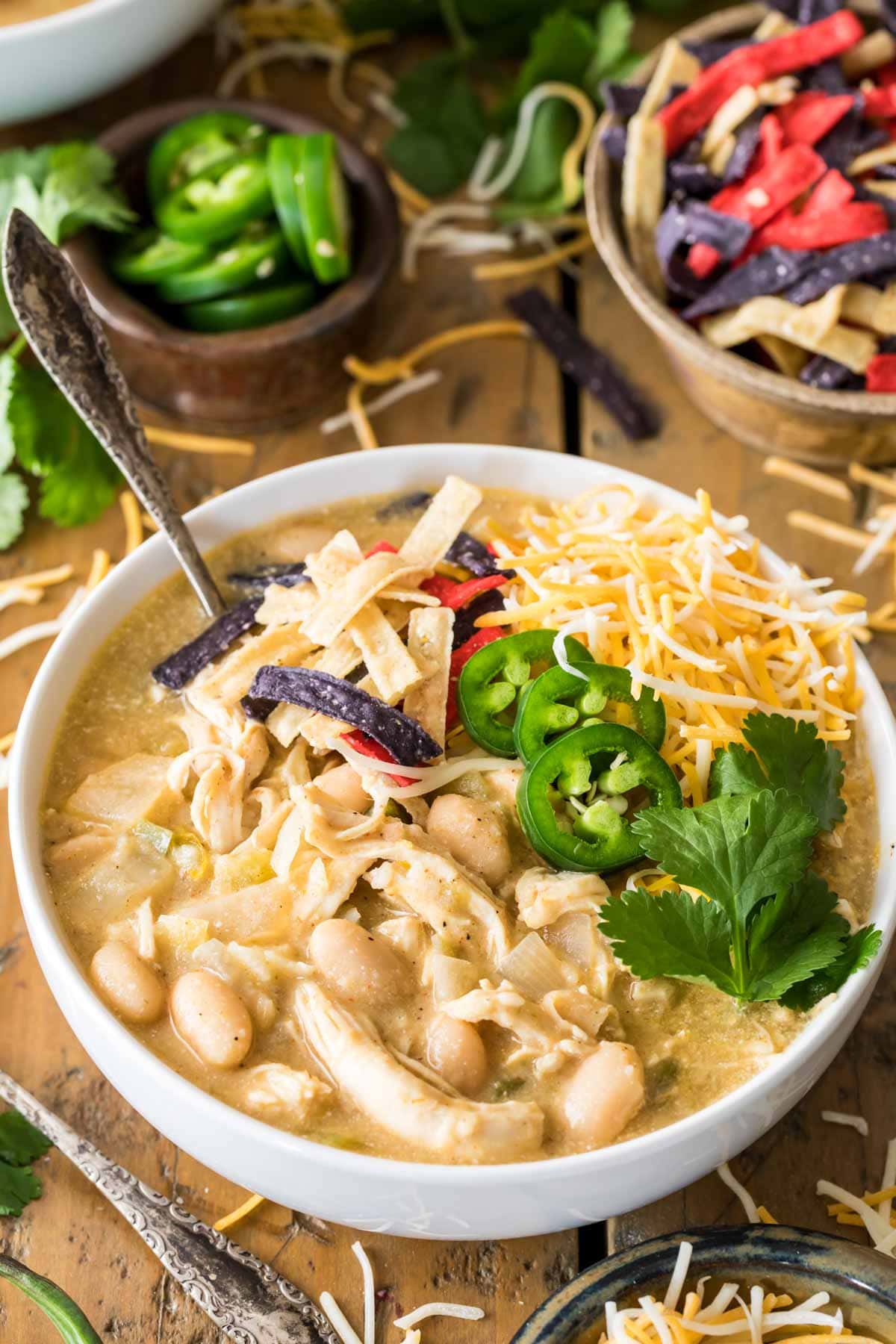 Bowl of white chicken chili topped with jalapeno, shredded tortillas, and cheese. 