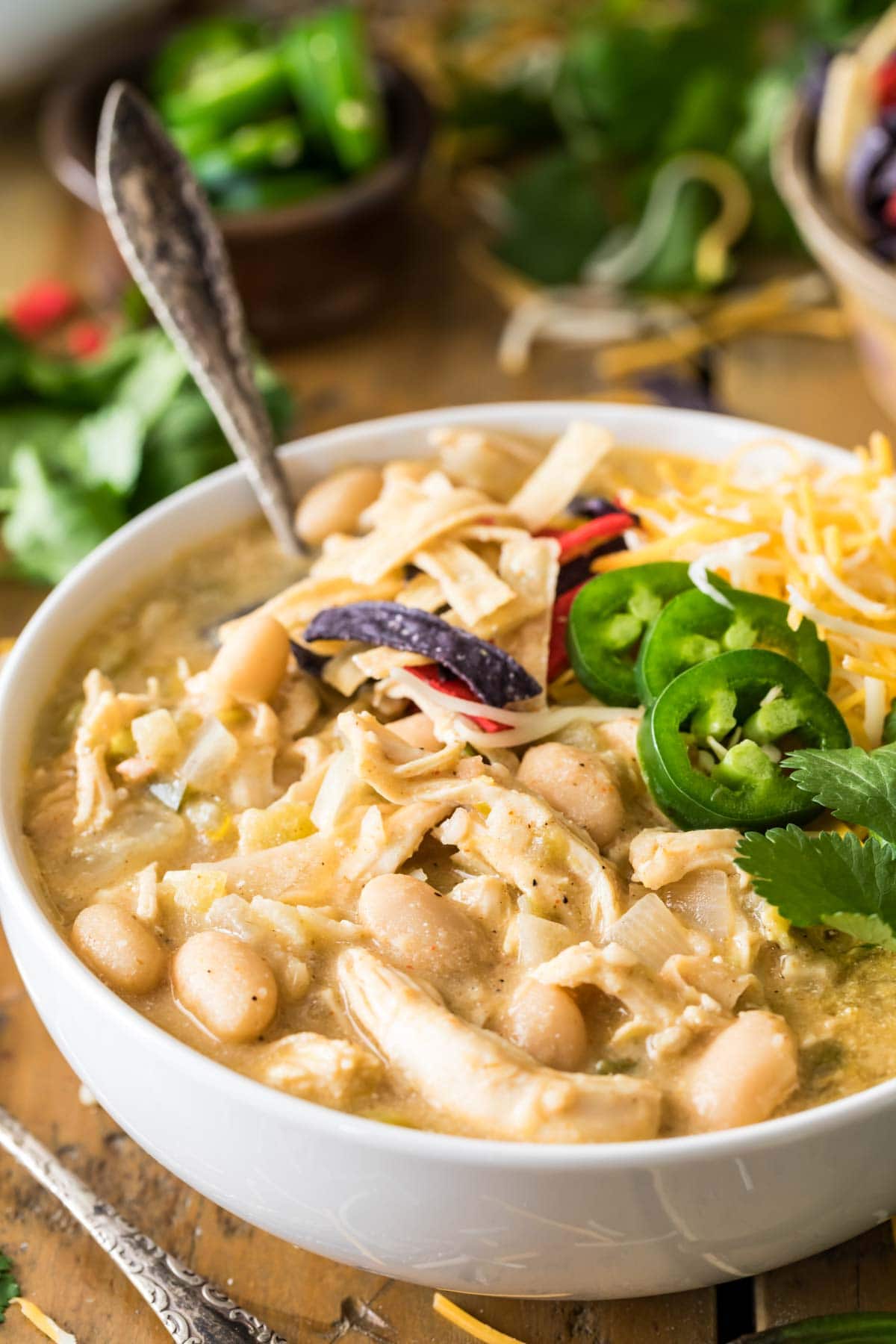 Bowl of white chili made with chicken and beans that's been topped with cilantro, jalapeno, tortilla strips, and cheese.