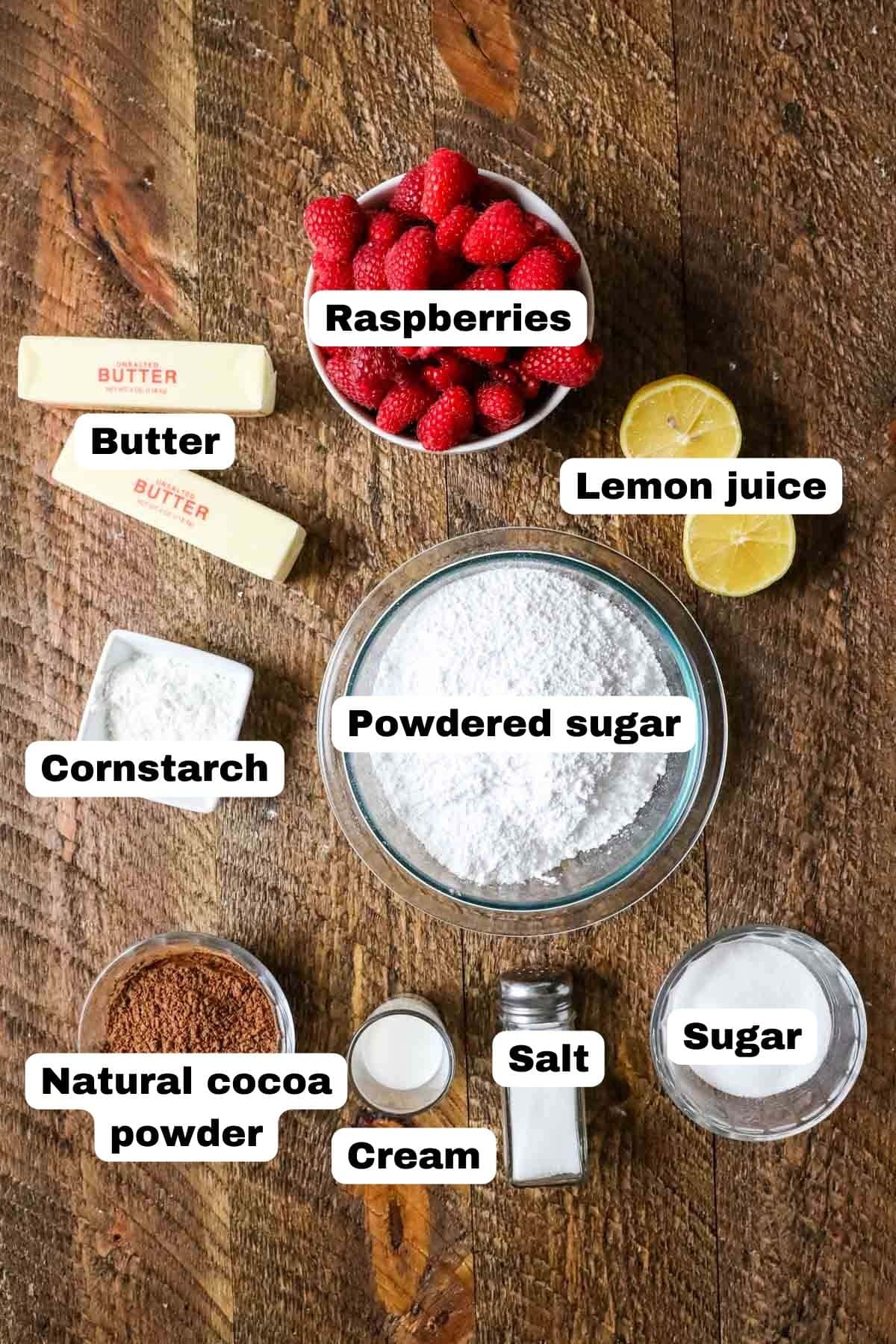 Overhead view of labelled ingredients including fresh raspberries, lemon halves, cocoa powder, and more.
