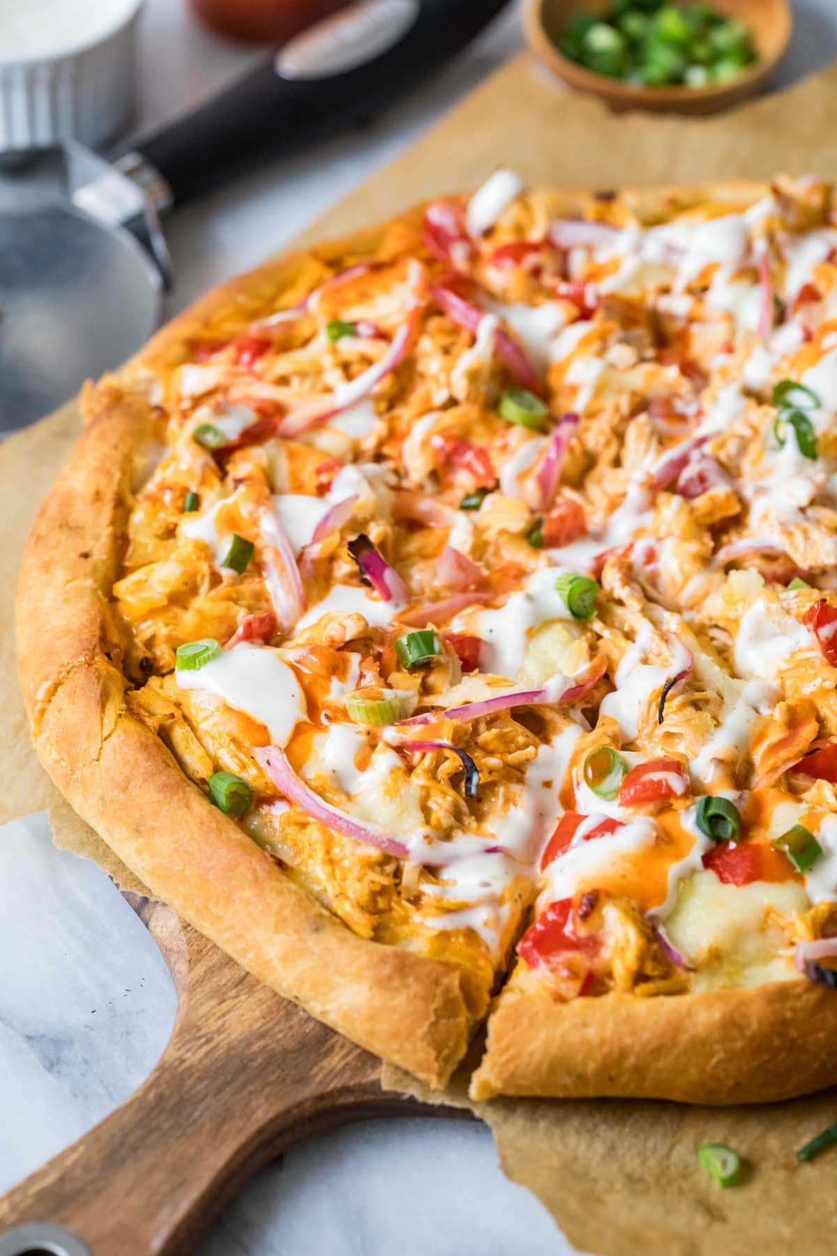 Overhead view of a buffalo chicken pizza made with red and green onion, ranch dressing, and diced tomatoes.