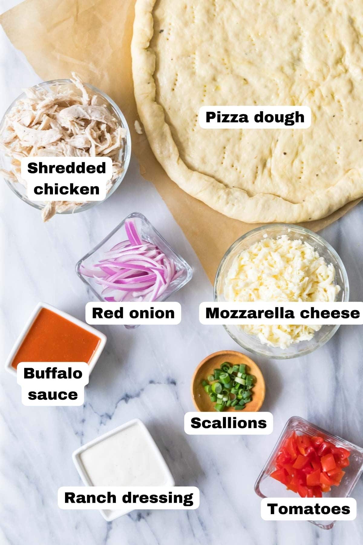 Overhead view of labelled ingredients including pizza dough, chicken, buffalo sauce, and more.