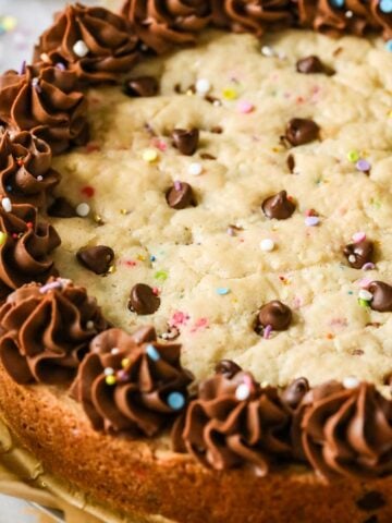 Close-up view of a chocolate chip cookie cake topped with a ring of chocolate frosting and sprinkles.
