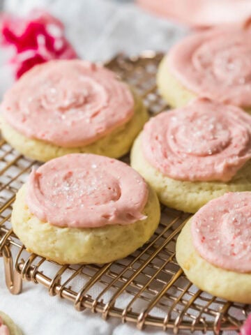 Sour cream cookies topped with a pale pink frosting on a cooling rack.