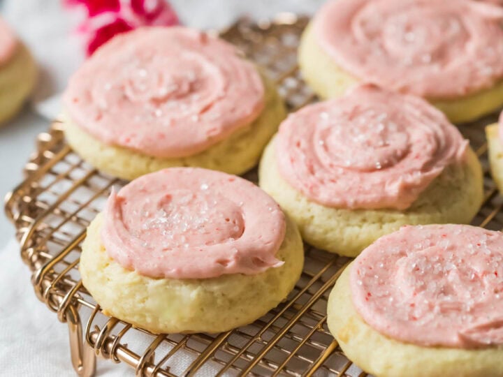 Sour cream cookies topped with a pale pink frosting on a cooling rack.