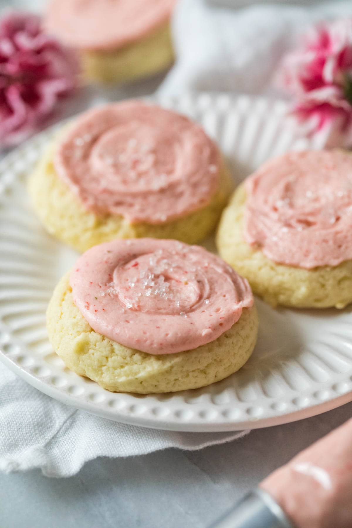 Plate of thick, cakey cookies topped with a pastel pink frosting.