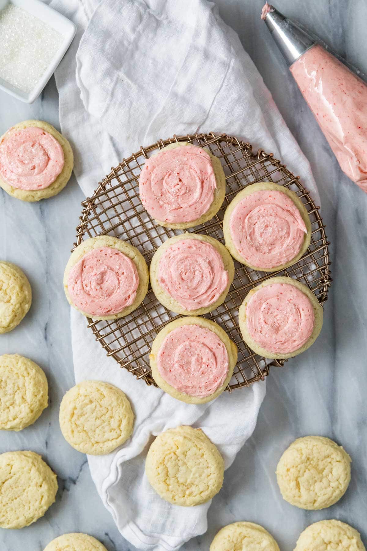 Overhead view of sour cream cookies topped with a pastel pink frosting on a round cooling rack.