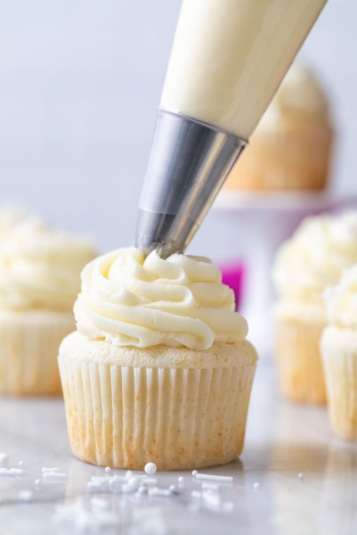 Vanilla frosting being piped on top of a white cupcake.