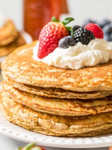 Stack of whole wheat pancakes topped with whipped cream and berries.