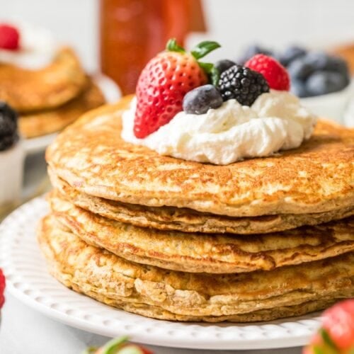 Stack of whole wheat pancakes topped with whipped cream and berries.