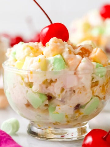 Glass bowl of ambrosia salad topped with a maraschino cherry.