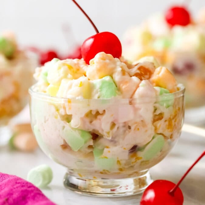 Glass bowl of ambrosia salad topped with a maraschino cherry.