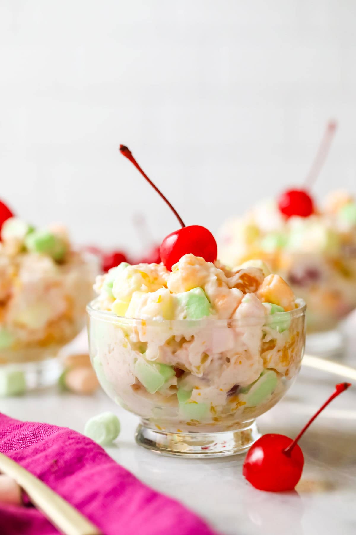 Glass bowl of ambrosia salad topped with a maraschino cherry.
