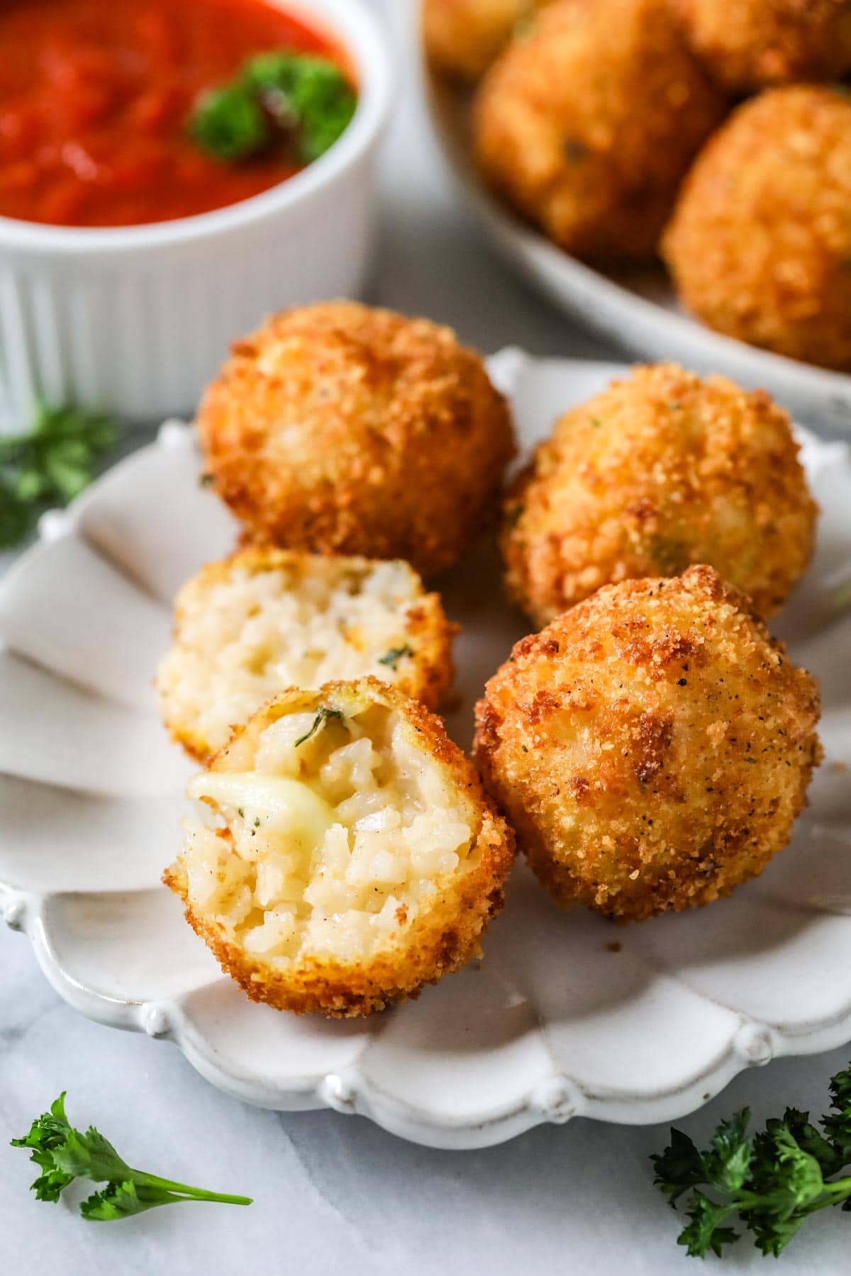 Arancini on a plate with one cut in half to show a cheesy filling.