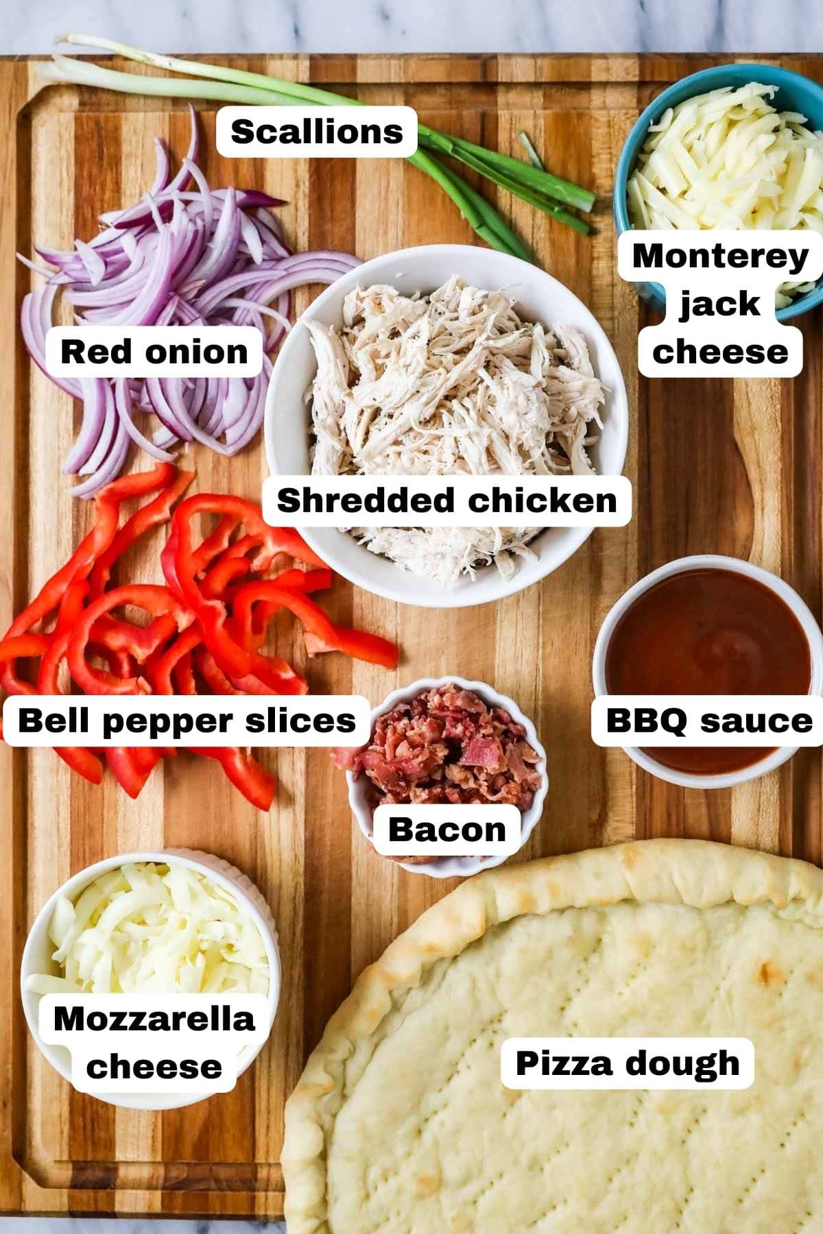 Overhead view of labelled ingredients including shredded chicken, pizza dough, bbq sauce, cheese, and more.