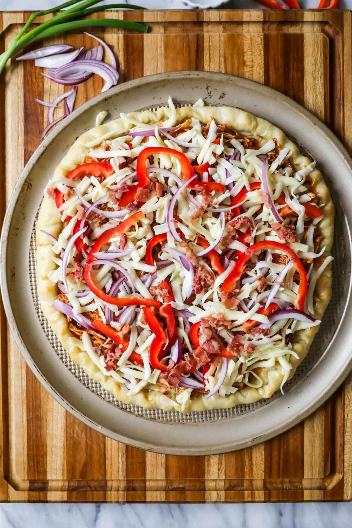 Overhead view of a pizza topped with BBQ chicken, cheese, peppers, and onions before baking.