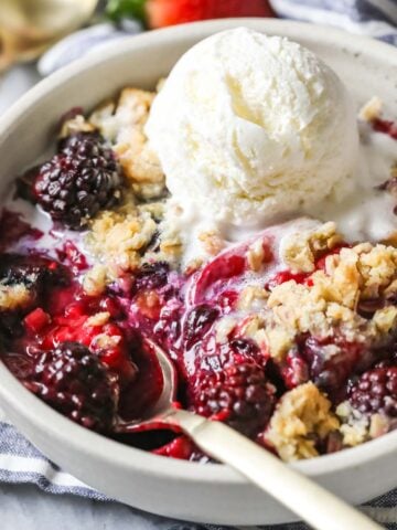 Bowl of berry crisp topped with a melting scoop of vanilla ice cream.