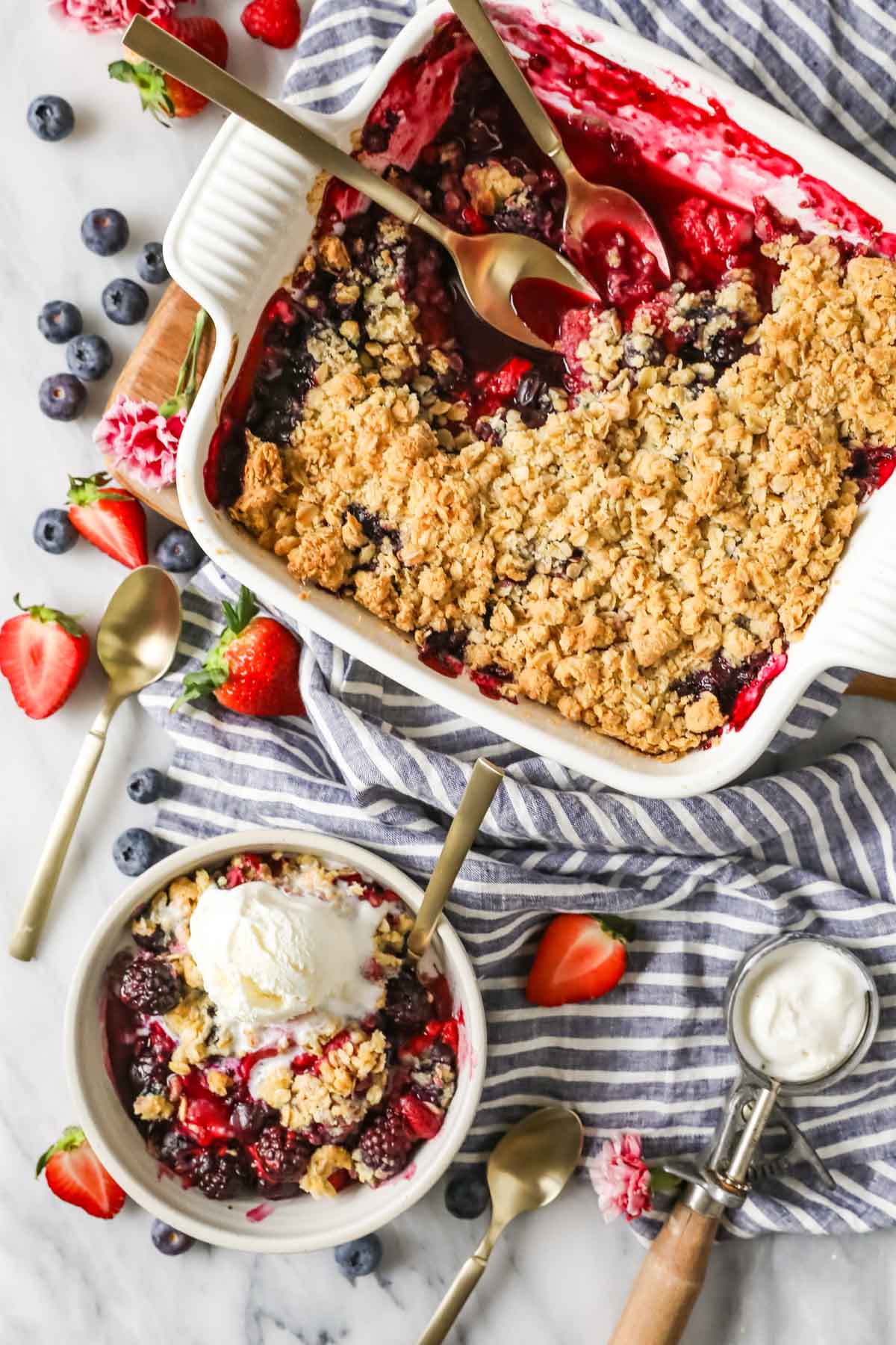 Overhead view of a berry crisp in a baking dish with a single serving in a bowl beside it.