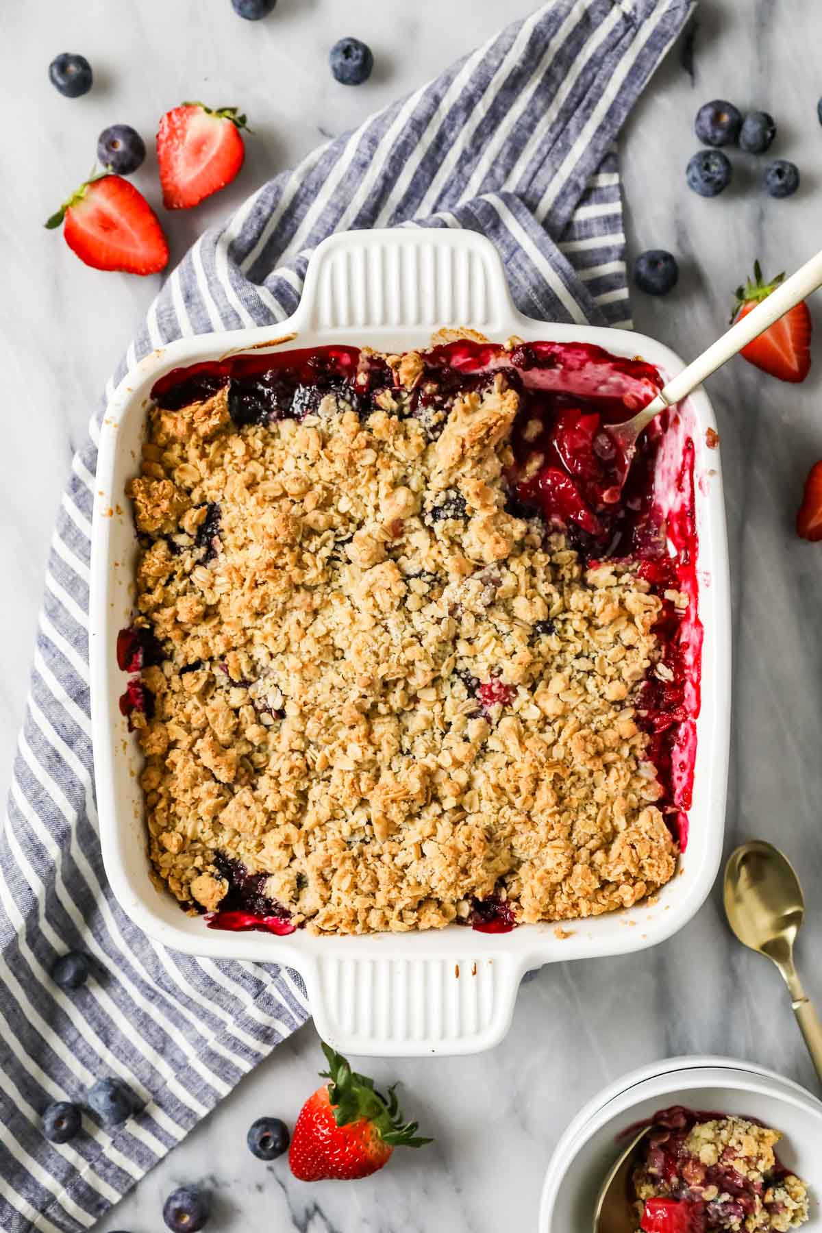 Overhead view of a square baking dish with a baked berry dessert topped with an oat crisp.