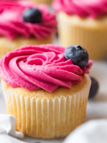Cupcake frosted with a vibrantly colored blueberry frosting rosette and a blueberry garnish.